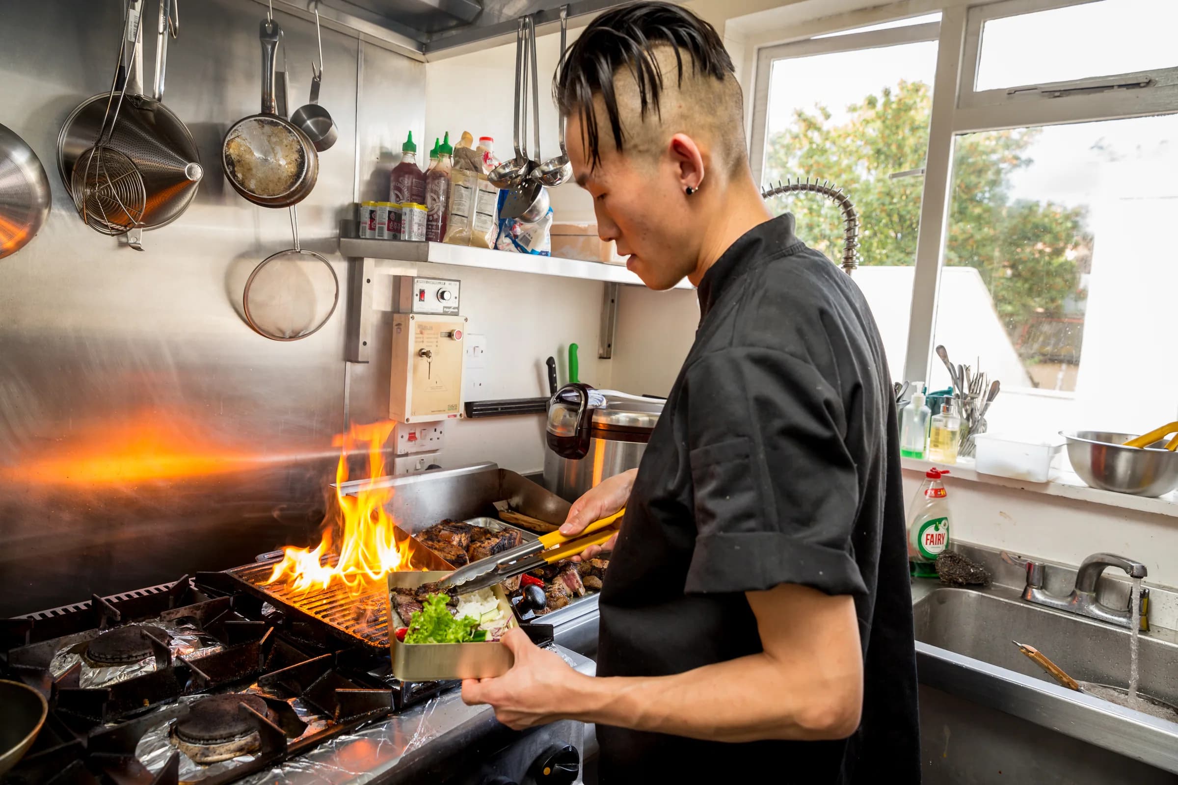 Private chef Teo Kim cooking over an open flame in a professional kitchen
